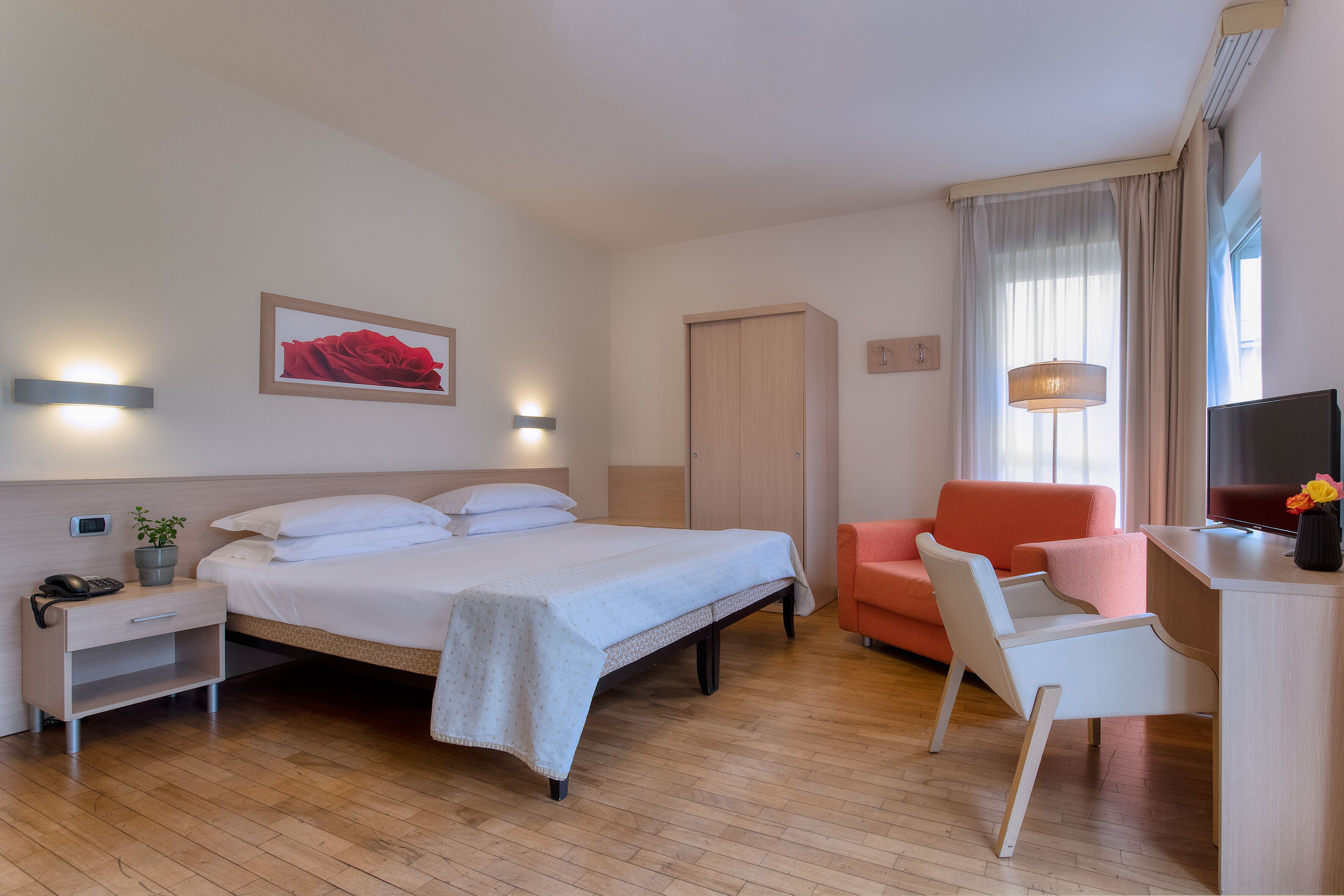 Een hotelkamer met een bed, een bureau, een stoel, een televisie, een lamp en een raam met gordijnen.