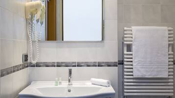A bathroom with a sink, a hairdryer mounted on the wall, a towel rack with a towel, and a window.