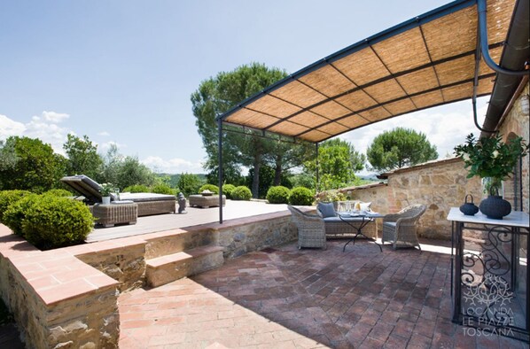 A patio area with outdoor furniture, a pergola providing shade, and a stone wall in the background.