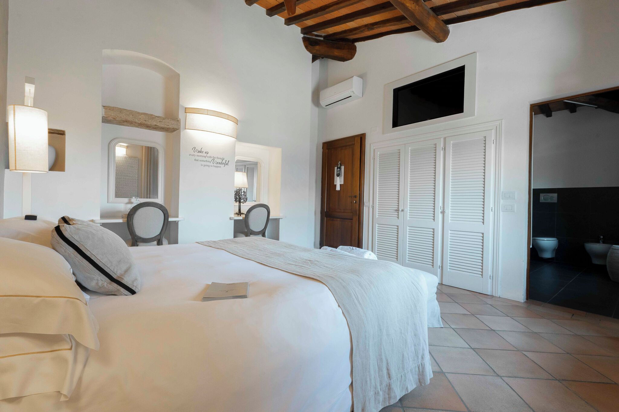 A hotel room with a large bed, a desk, a mirror, and a bathroom visible through an open door.