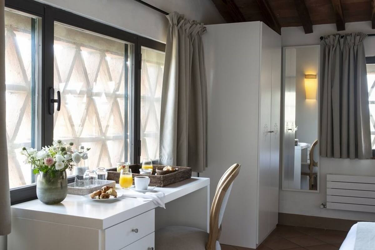 Une chambre à coucher avec un lit, un bureau avec des articles pour le petit-déjeuner, une chaise et une fenêtre avec des rideaux.