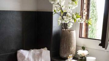 A modern bathroom with a bathtub, a large vase with white flowers, a towel, and a window with a view of greenery.