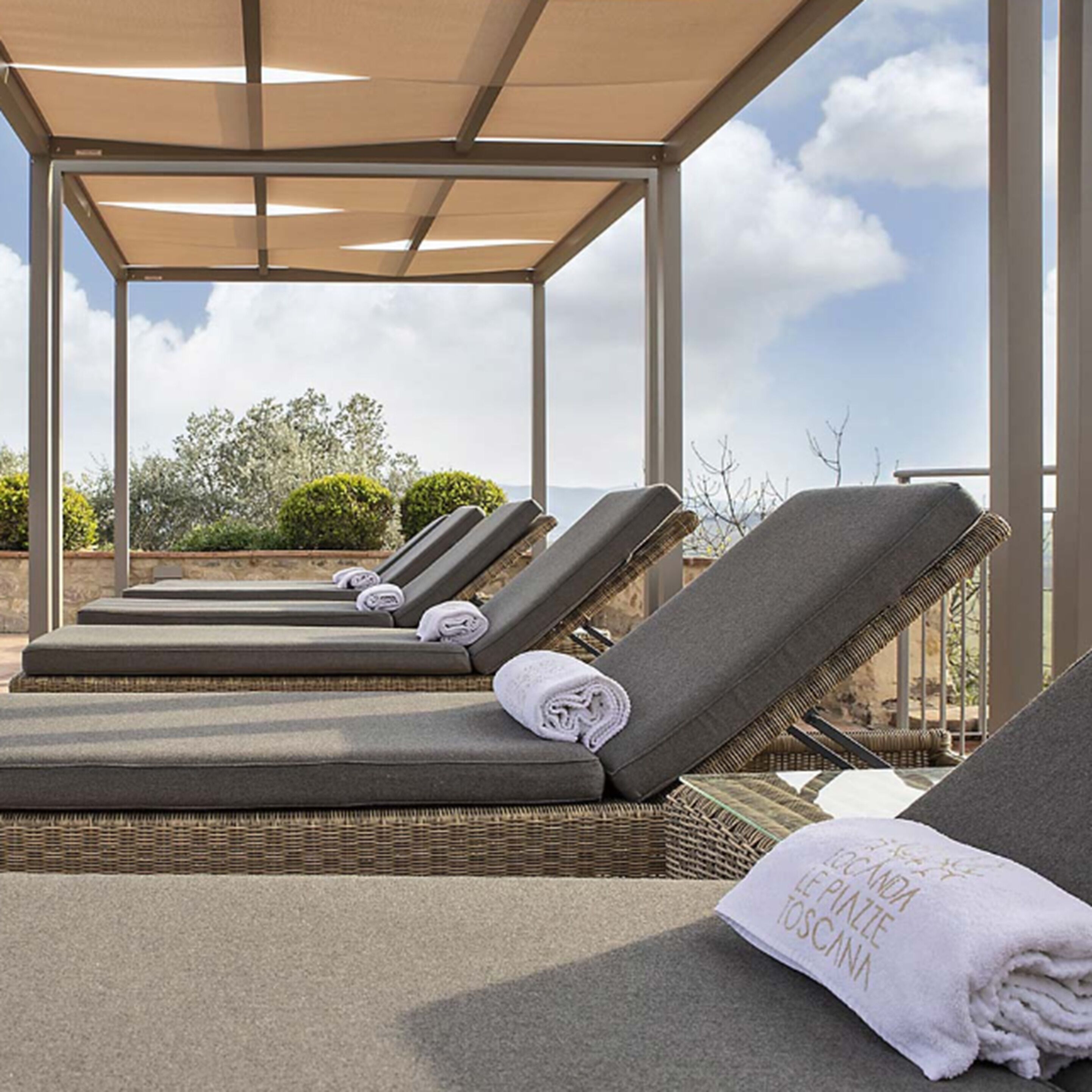 A rooftop lounge area with sun loungers, a pergola, and a view of the sky and landscape.