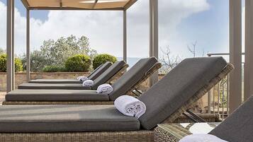 A rooftop lounge area with sun loungers, a pergola, and a view of the sky and landscape.