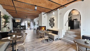 Un vaste espace de salle à manger avec des tables et des chaises en bois, une cheminée et, au fond, une cuisine moderne.