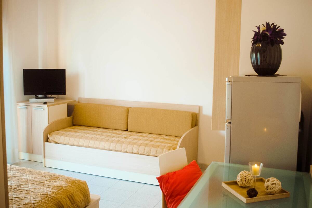Una habitación compacta con cama, sofá, una mesita con una vela y televisión sobre un mueble.