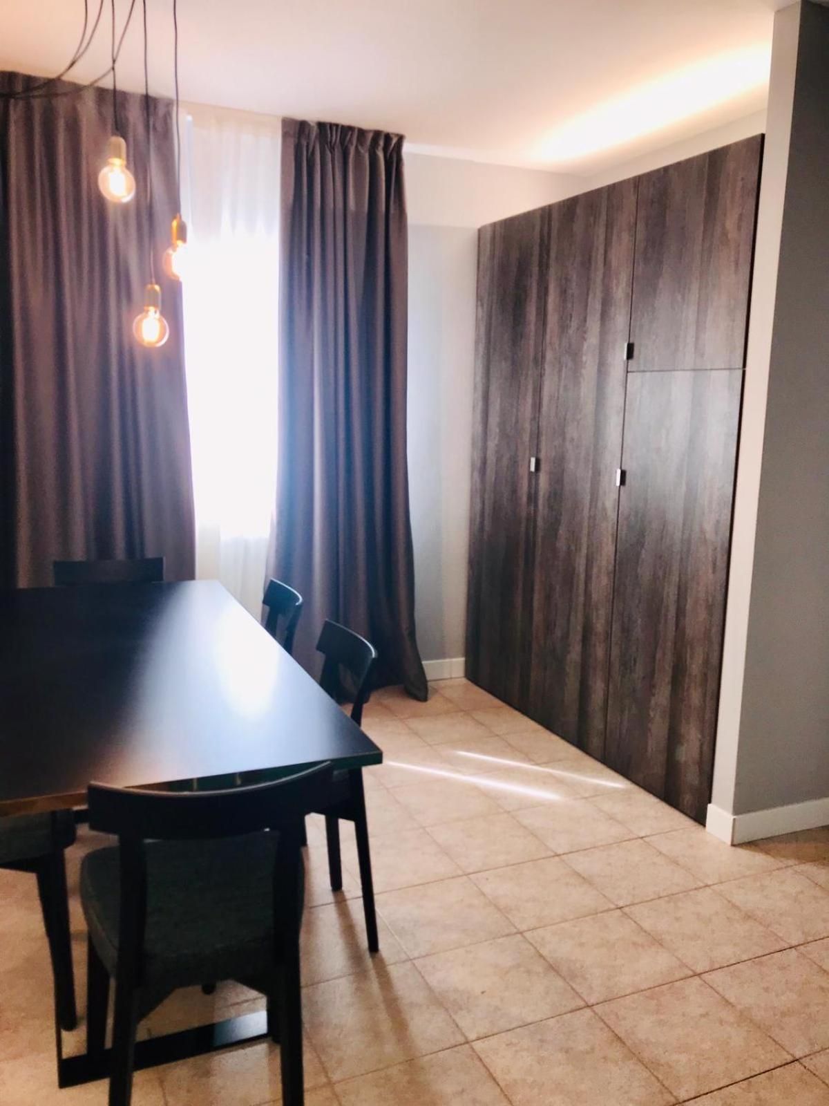A dining area with a dark wooden table and chairs, a large window with curtains, and a wardrobe with dark wood panels.