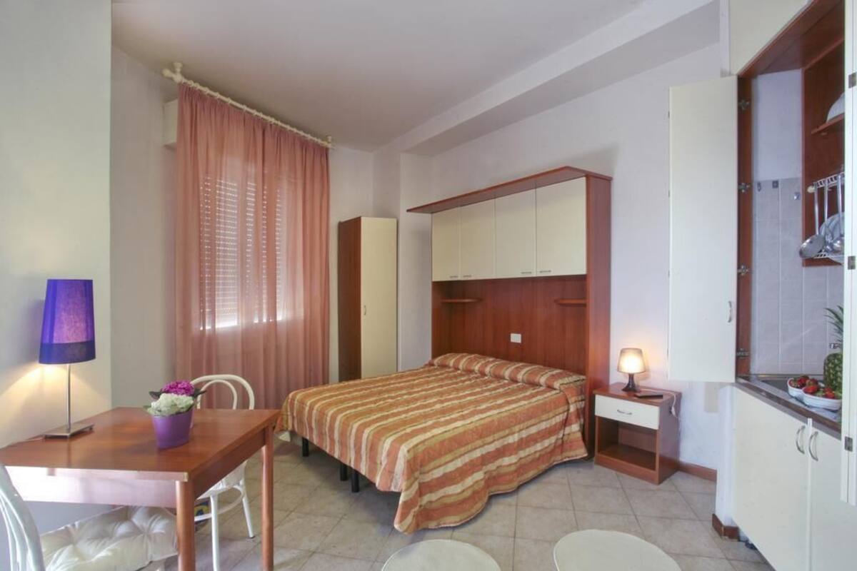 A bedroom with a bed, a desk, a chair, a nightstand, and a mirror.