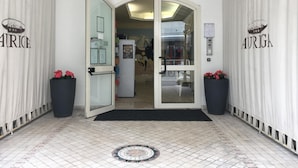 A hotel entrance with a glass door, name signage, and potted plants. - Residence Auriga (Rimini)
