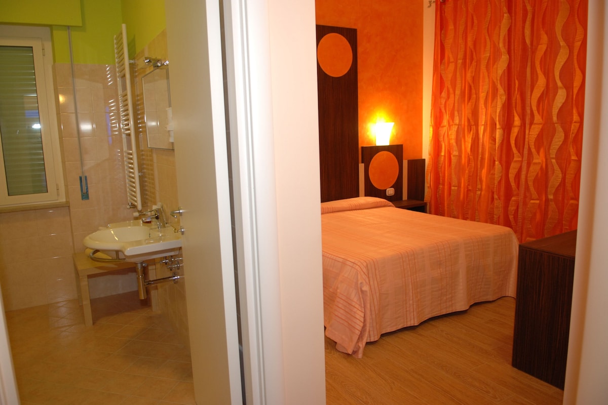 Un dormitorio con cama, mesita de noche, espejo y lámpara de pared.