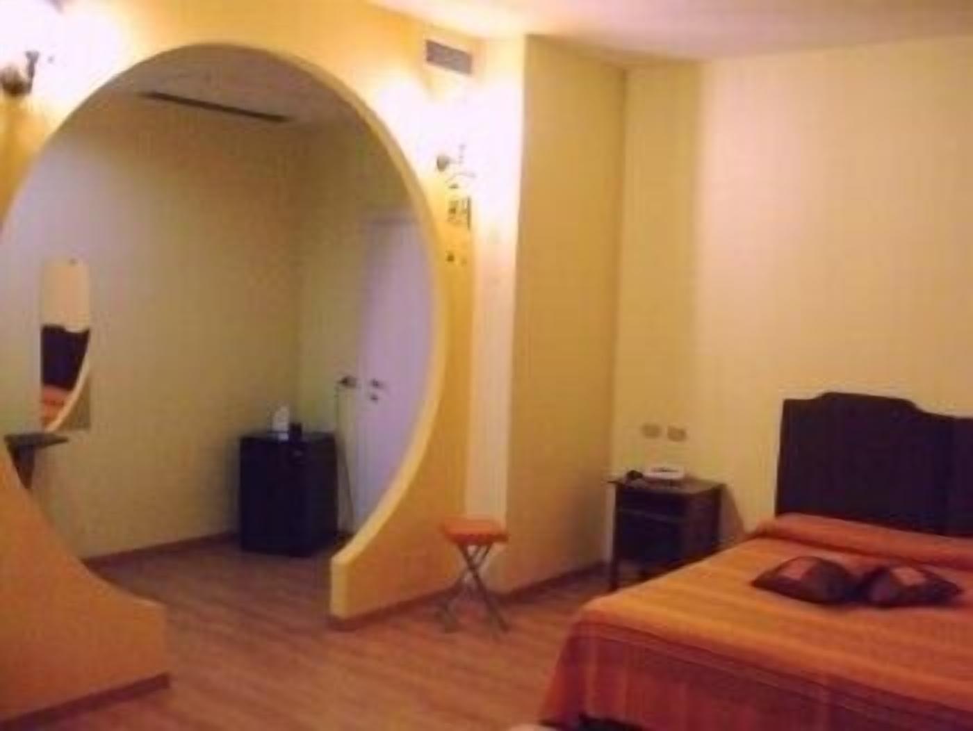 A hotel room with a curved doorway leading to a bathroom, a bed with a headboard, a small table, and a chair.