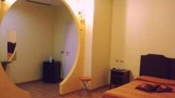 A hotel room with a curved doorway leading to a bathroom, a bed with a headboard, a small table, and a chair.