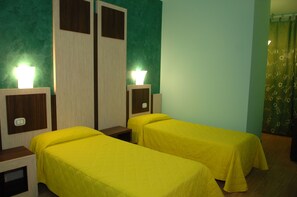 Una habitación con dos camas individuales, cada una con cabecera de madera y mesita de noche. Hay dos lámparas de pared en las cabeceras.