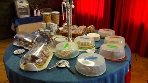 Una mesa de bufé con diferentes alimentos y utensilios, cubierta con campanas de plástico, con un fondo de cortina roja.