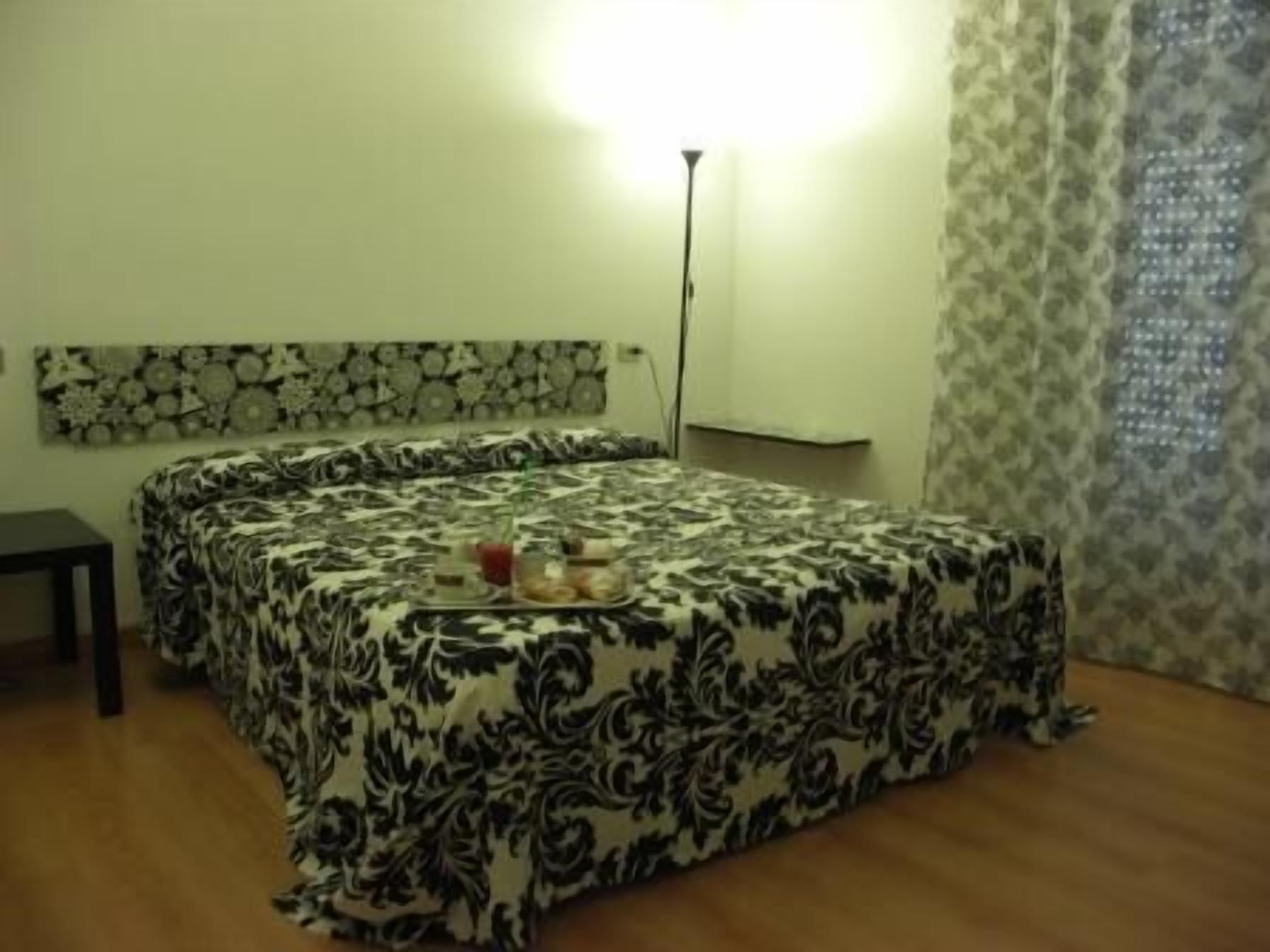 Ein Hotelzimmer mit einem geblümten Bettüberwurf, einem Nachttisch, einer Lampe und einem Wandbild.