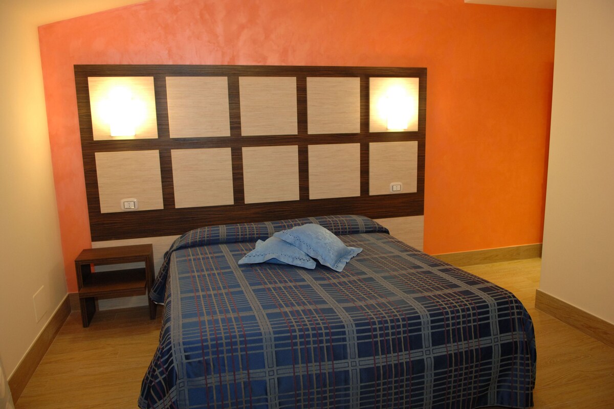 Un dormitorio con cabecera de madera, colcha a cuadros azules y dos lámparas de noche.