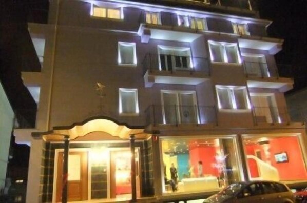 Un hotel de varios pisos con ventanas iluminadas y una entrada principal en la planta baja, muy luminosa.