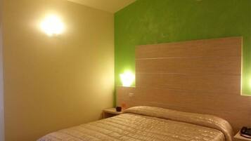 Een hotelkamer met een bed, nachtkastje en een lampje aan de muur.