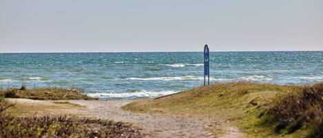 A coastal path leading to the sea with a signpost in the distance.