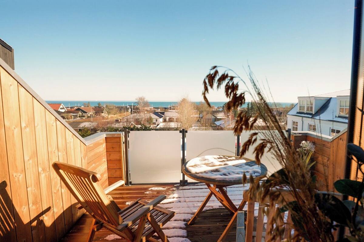 A wooden deck with a table and chairs, overlooking a coastal town.