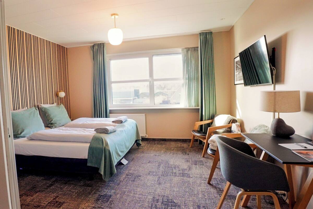 A hotel room with a bed, a desk with a chair, a television, and a window with curtains.