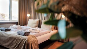 Una cama bien hecha con toallas, una ventana con cortinas y una pared con l íneas verticales y luces empotradas.