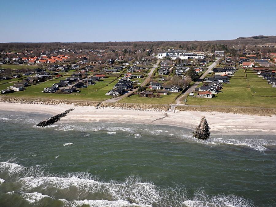 An aerial view of a coastal town with houses, a beach, and wind turbines in the distance.