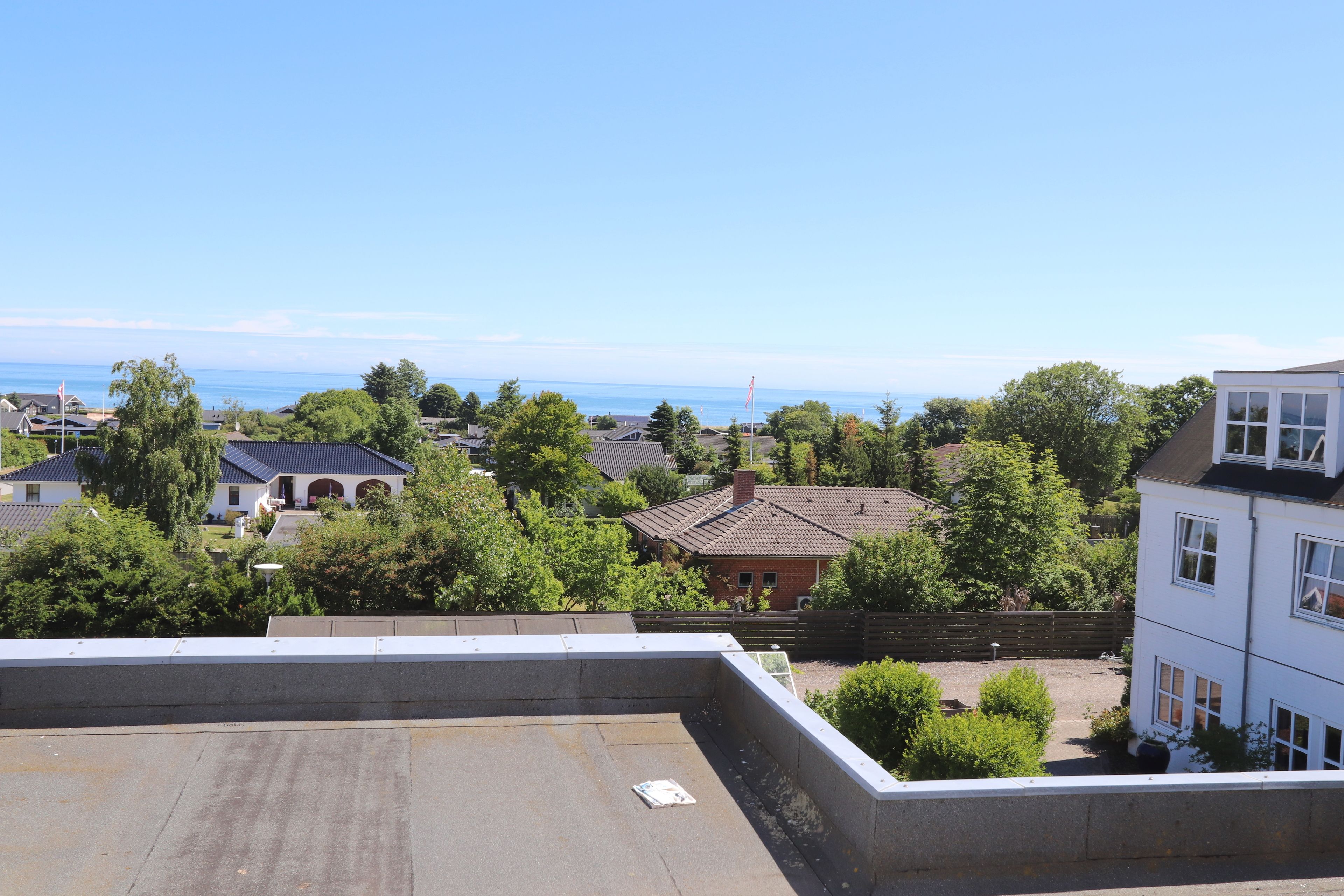 A residential area with houses, trees, and a clear view of the sea.
