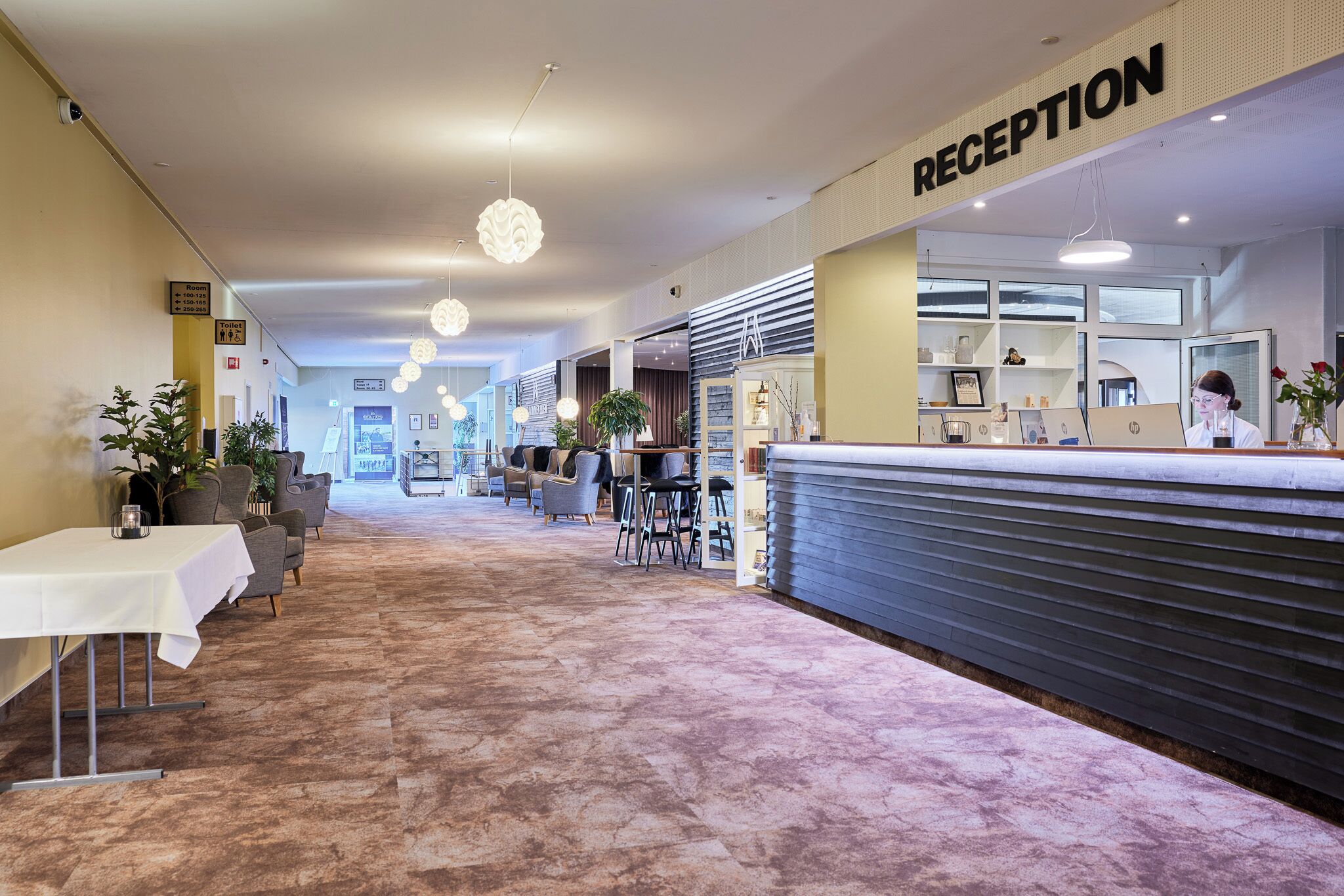 Zona de recepción de un hotel con mostrador, área de descanso y piso alfombrado.