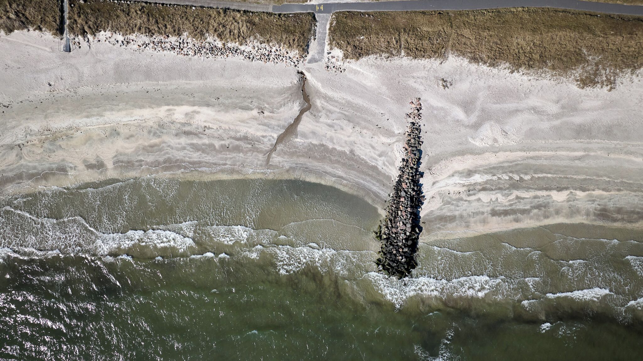 An aerial view of a salt flat with a large salt formation and a narrow water channel.