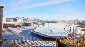 Un jacuzzi en una terraza de madera con vista a la playa y edificios al fondo.