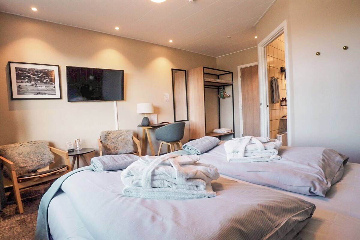 A hotel room with two beds, a desk, a chair, and a bathroom visible through an open door.