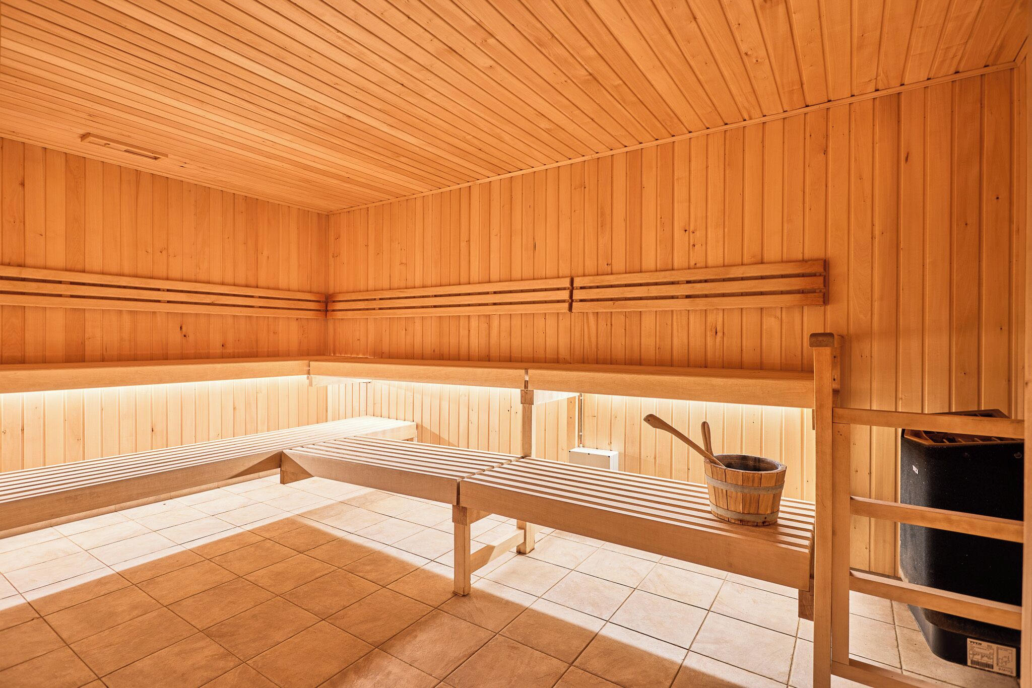 Un sauna avec des bancs en bois et un banc en bois avec un seau.