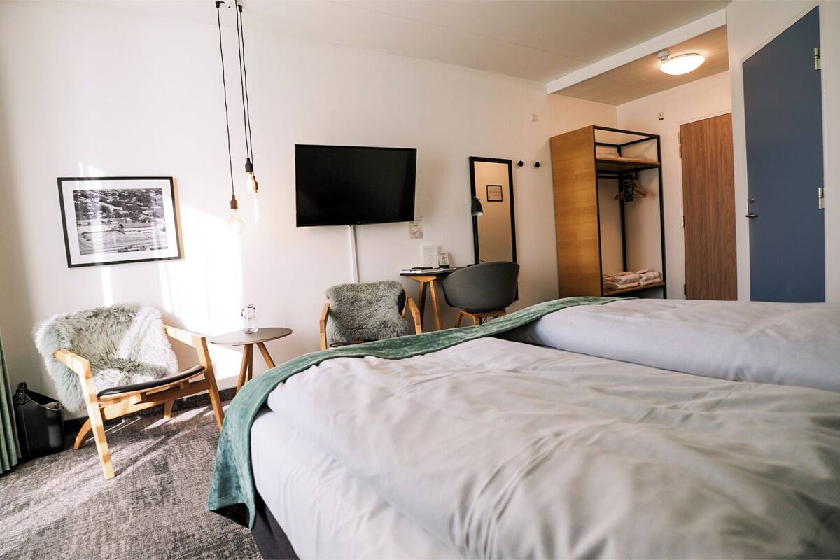 A hotel room with a large bed, a chair, a small table, a TV, and a wardrobe.