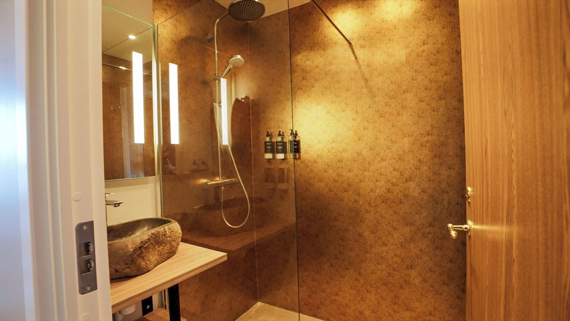 A modern bathroom with a glass-enclosed shower, a wooden vanity, and a mirror.