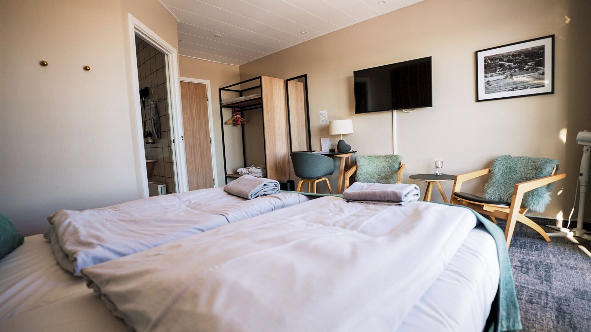 Ein Hotelzimmer mit zwei Betten, einem Schreibtisch, einem Stuhl, einem Fernseher und einem gerahmten Bild an der Wand.