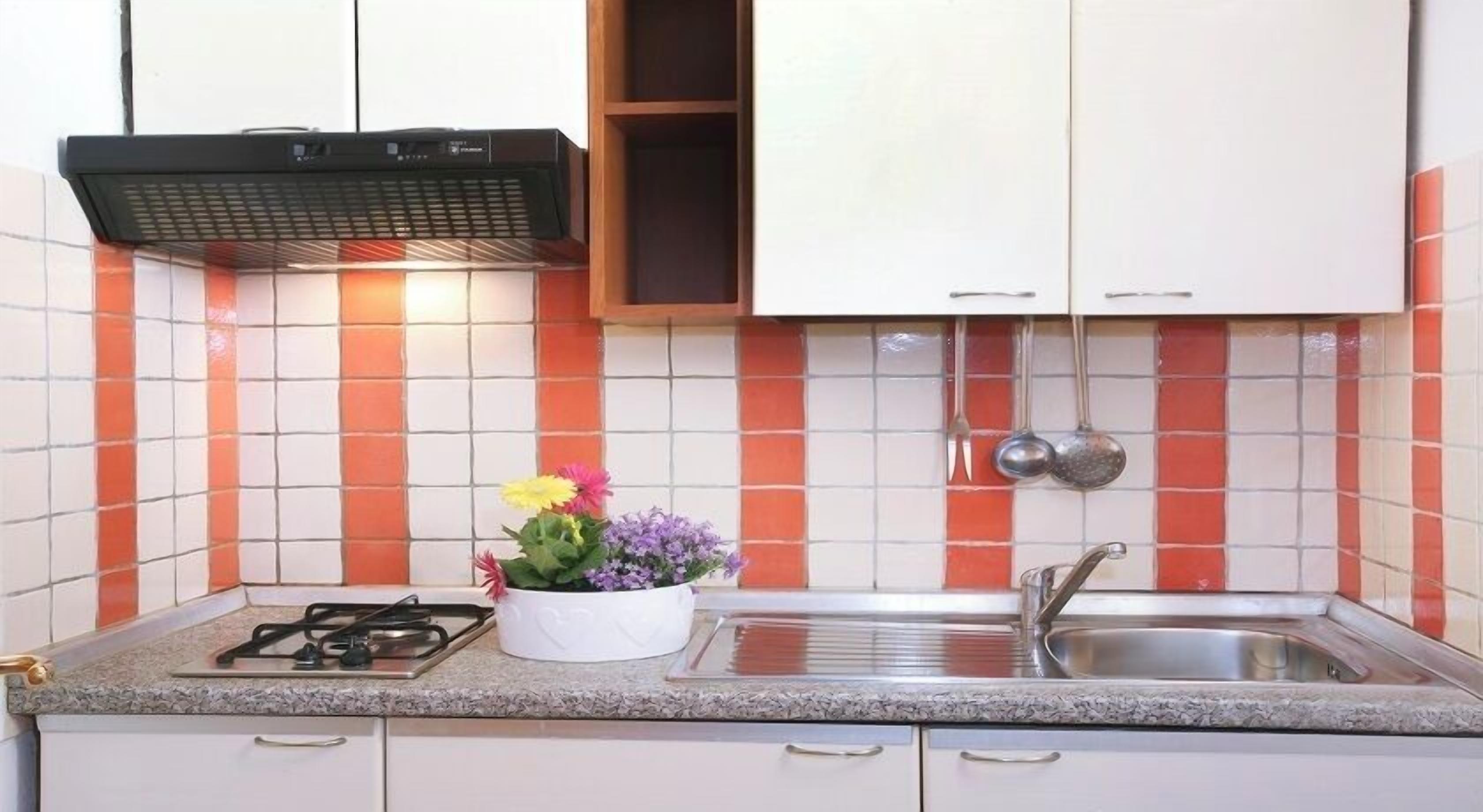 Een keuken met een gasfornuis, een spoelbak en een bloevas.