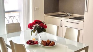 Une cuisine moderne avec des meubles blancs, un évier en acier inoxydable et une table à manger en verre, accompagnée de quatre chaises.
