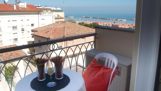 Un balcon avec une table, deux chaises et une vue sur la mer et les bâtiments.