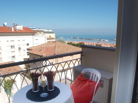 A balcony with a table, two chairs, and a view of the sea and buildings.