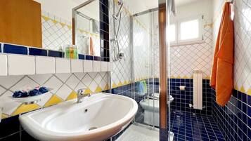 Une salle de bain avec un lavabo blanc, une cabine de douche en verre et des carreaux aux motifs bleus et jaunes.
