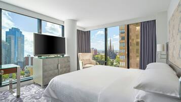 A hotel room with a large bed, a flat-screen TV, a desk, and a view of the cityscape.