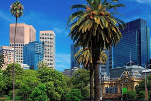A cityscape with modern high-rise buildings, a prominent palm tree, and a historic building with ornate architecture. - Sheraton Melbourne Hotel (Melbourne)