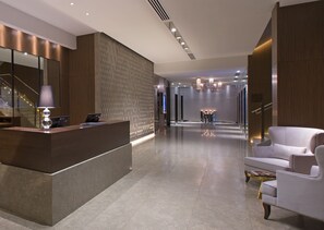 A modern reception area with a reception desk, a seating area with a white armchair, and a staircase in the background. - Sheraton Melbourne Hotel (Melbourne)