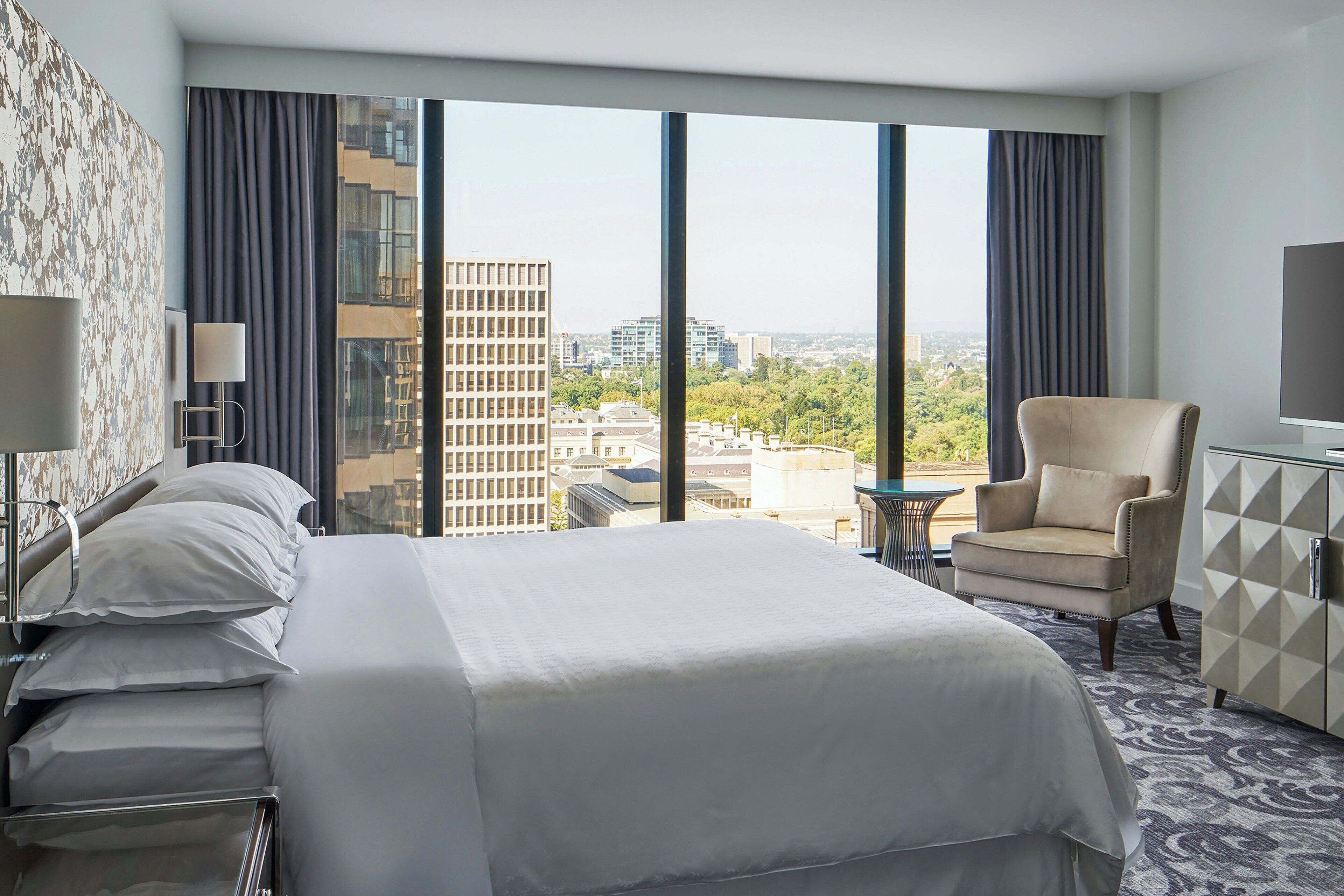 Une chambre d’hôtel avec un grand lit, une chaise, une petite table et un téléviseur.