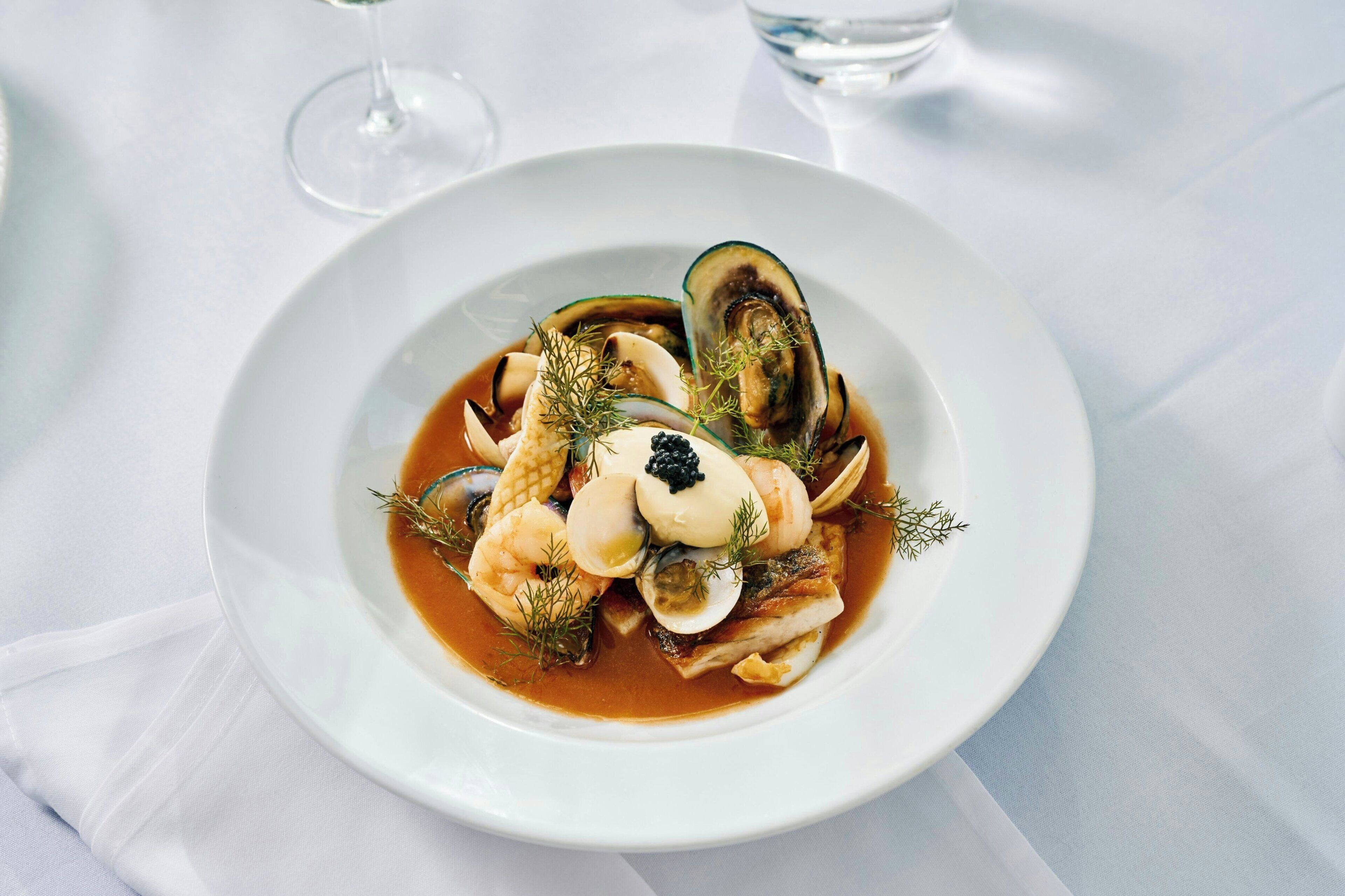 Un plato de mariscos sobre una vajilla blanca, con un vaso de agua al fondo.