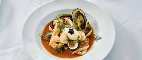 Un plato de mariscos sobre una vajilla blanca, con un vaso de agua al fondo.