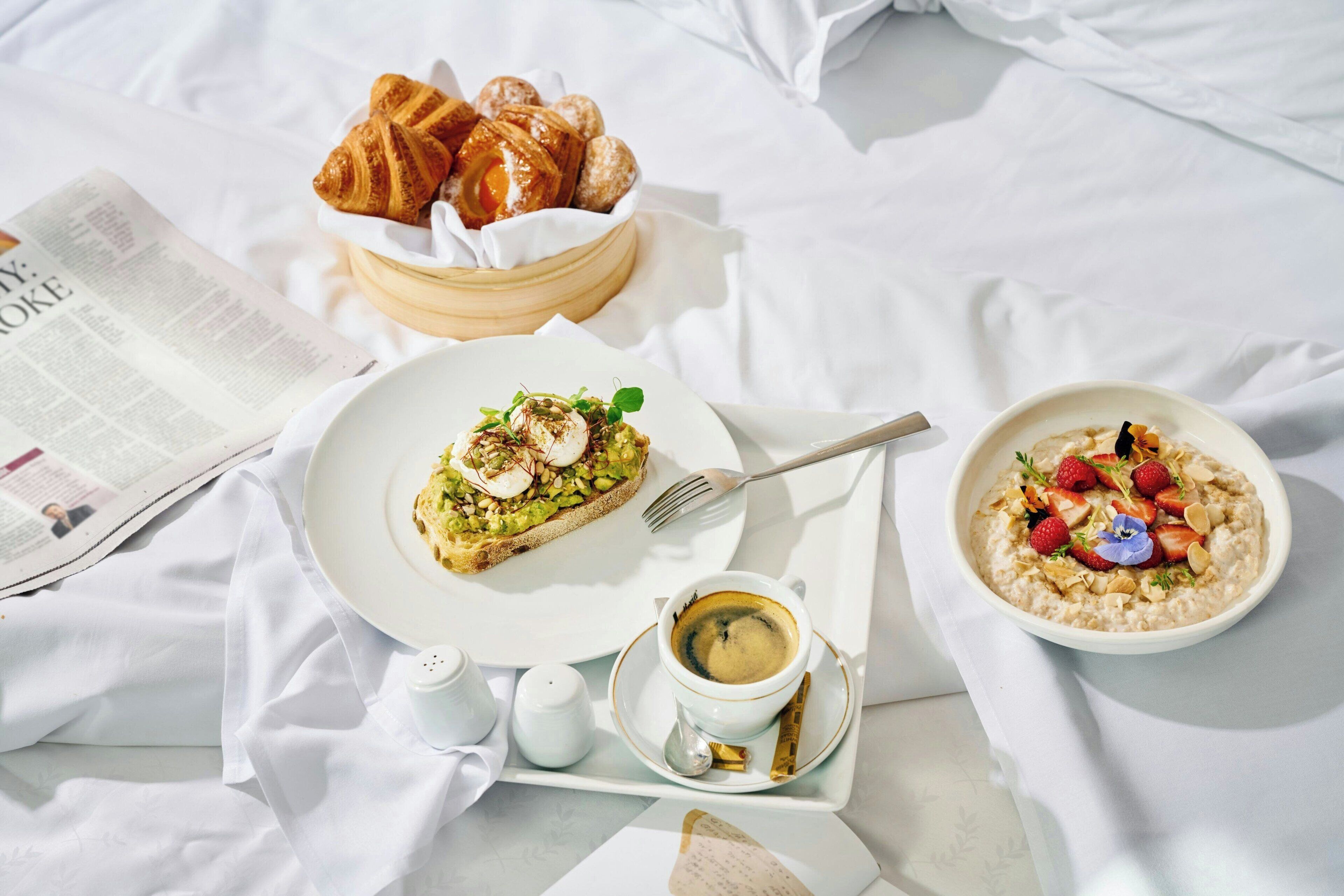 Un plateau de petit-déjeuner avec des croissants, des toasts, du porridge et du café, posé sur une table avec un journal.
