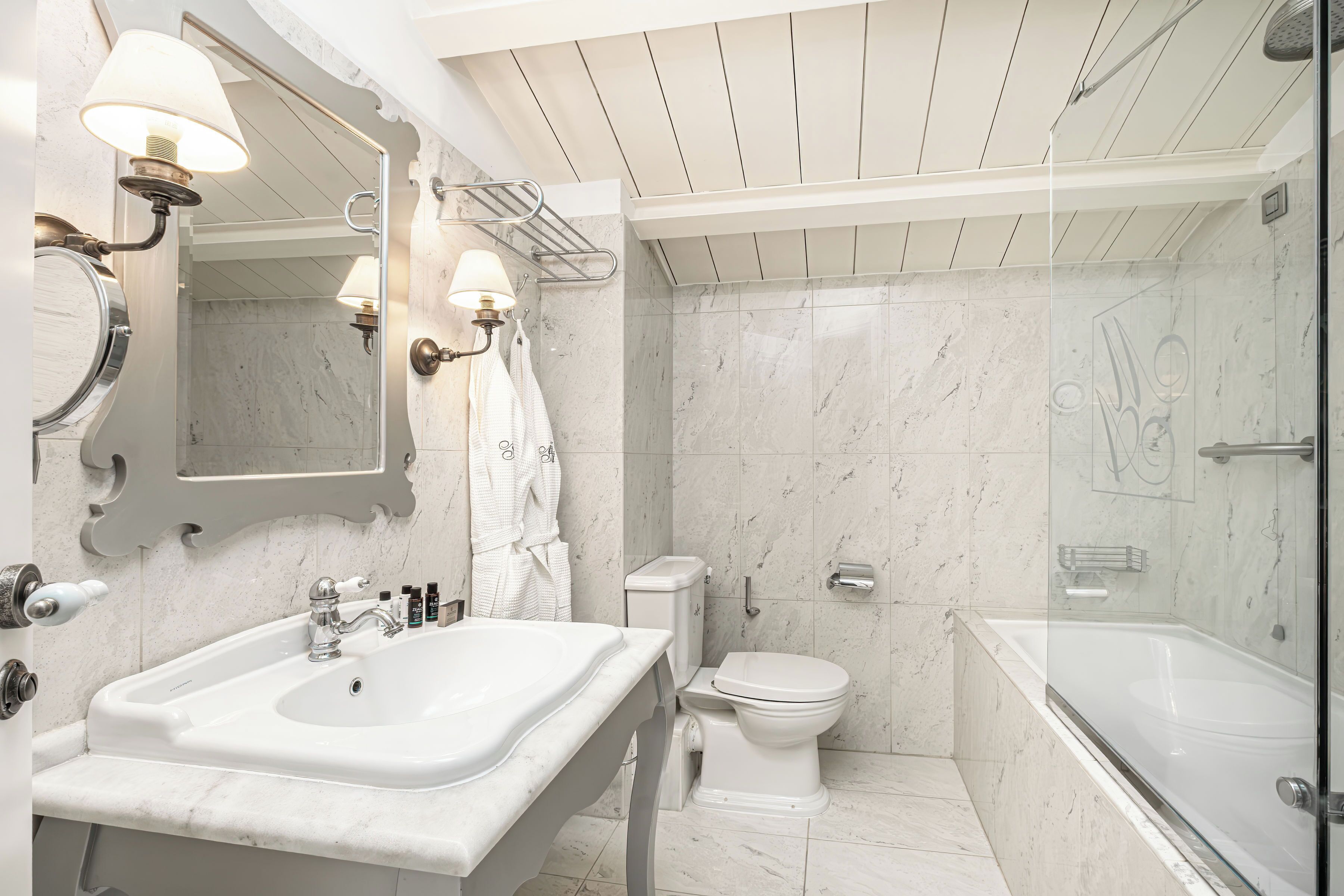 A modern bathroom with a marble sink, a toilet, and a glass-enclosed shower.