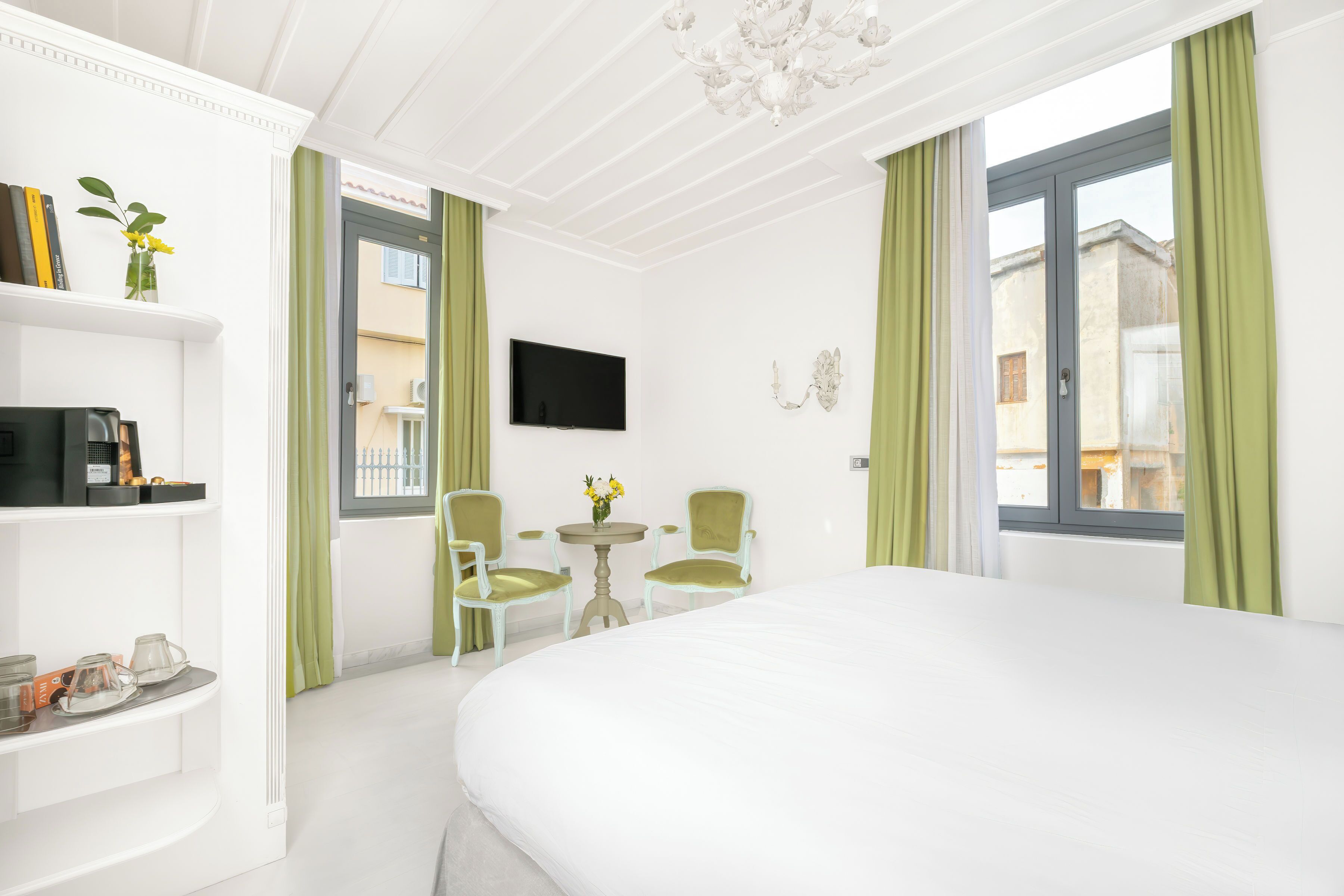 A hotel room with a large bed, a TV mounted on the wall, a small table with chairs, and a window with curtains.